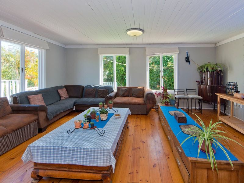 Spacious living room featuring polished timber flooring, a classic tongue and groove ceiling, and large windows providing ample natural light.