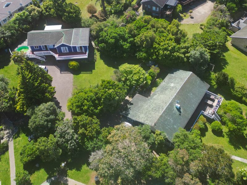 Aerial view of a residential property featuring a main house with a swimming pool, expansive garden, and paved driveway surrounded by mature trees.
