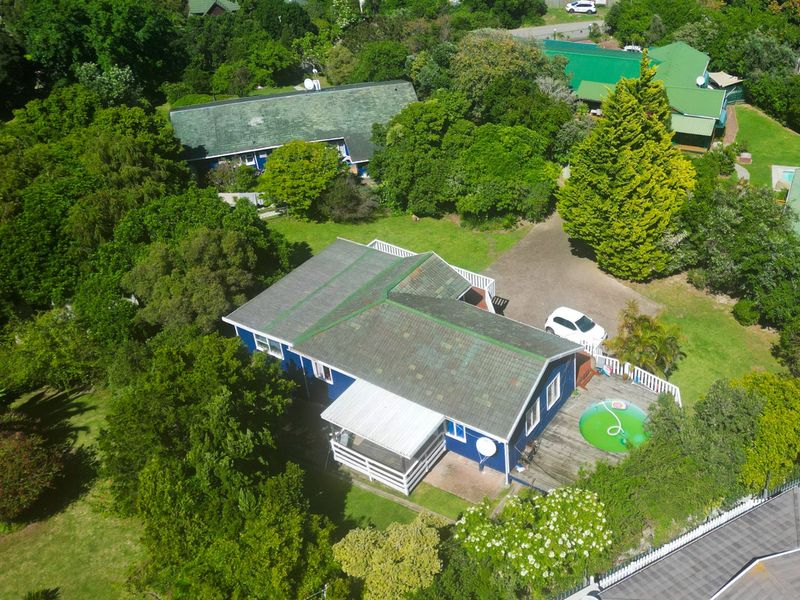 Aerial view of a detached house featuring a pitched roof, covered patio, wooden decking, and surrounding garden area within a residential setting.