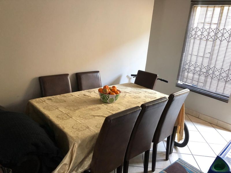 A functional dining area featuring tiled flooring and a window fitted with venetian blinds and a security gate.