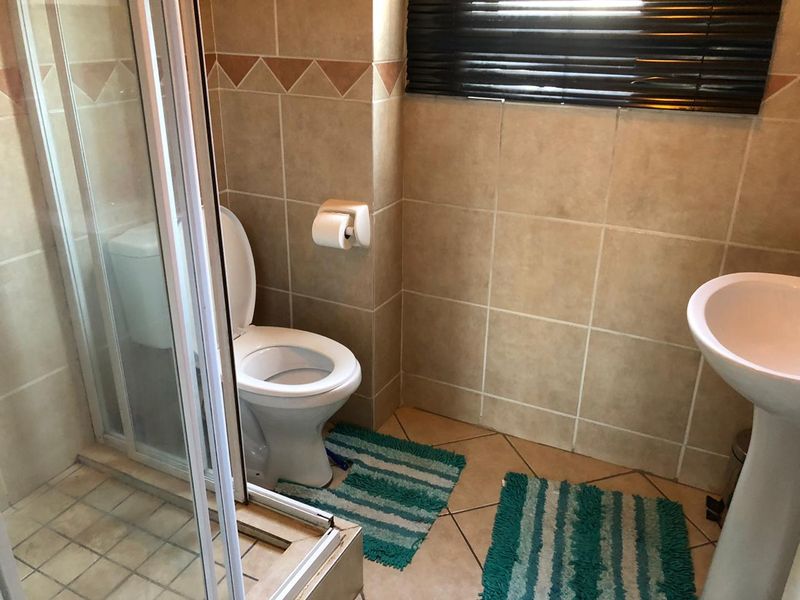 A functional bathroom featuring a shower enclosure, pedestal basin, and toilet with neutral wall and floor tiling.