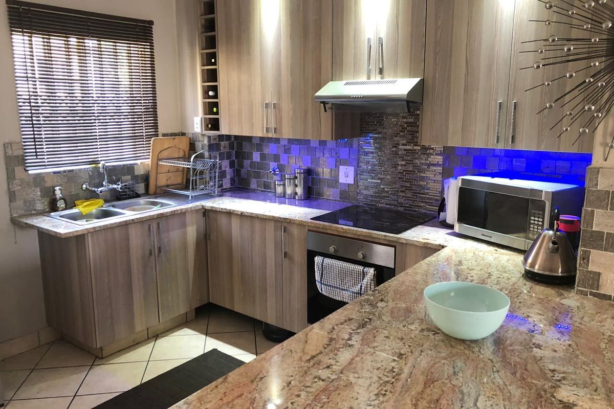 Modern kitchen featuring wood-grain cabinetry, granite countertops, mosaic tile backsplash, and integrated stainless steel appliances including an oven, hob, and extractor fan.
