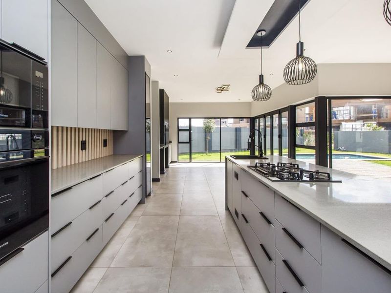 Modern open-plan kitchen featuring sleek grey cabinetry, stone countertops, a central island with a gas hob, and large sliding doors opening to the garden.