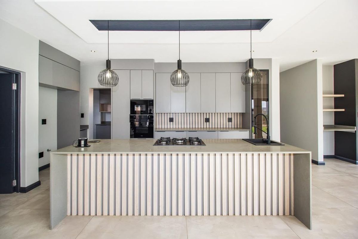 Modern kitchen featuring a large island with stone countertops, integrated cabinetry, built-in oven, gas hob, and stylish pendant lighting in a clean, contemporary space.