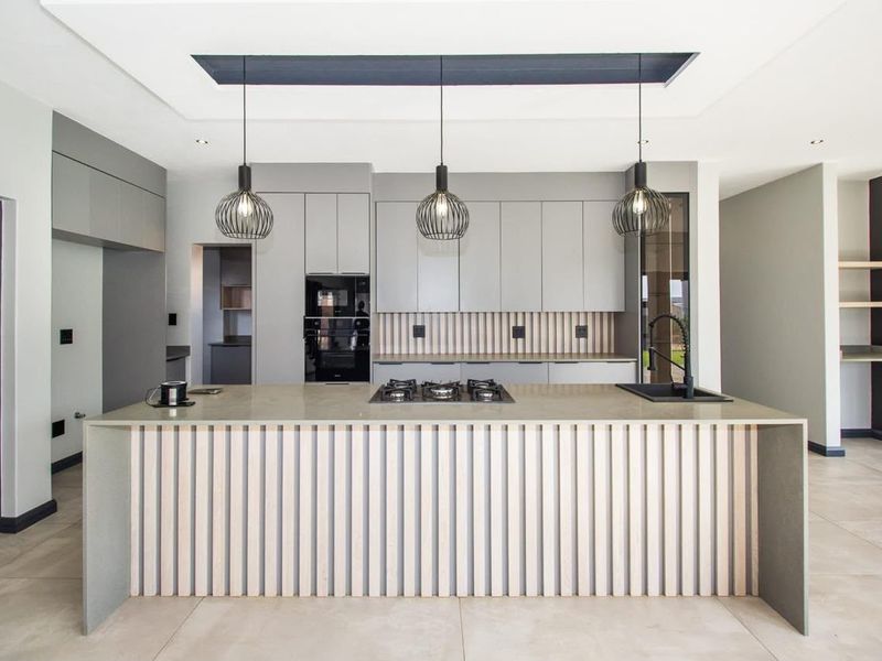 Modern kitchen featuring a large island with stone countertops, integrated cabinetry, built-in oven, gas hob, and stylish pendant lighting in a clean, contemporary space.