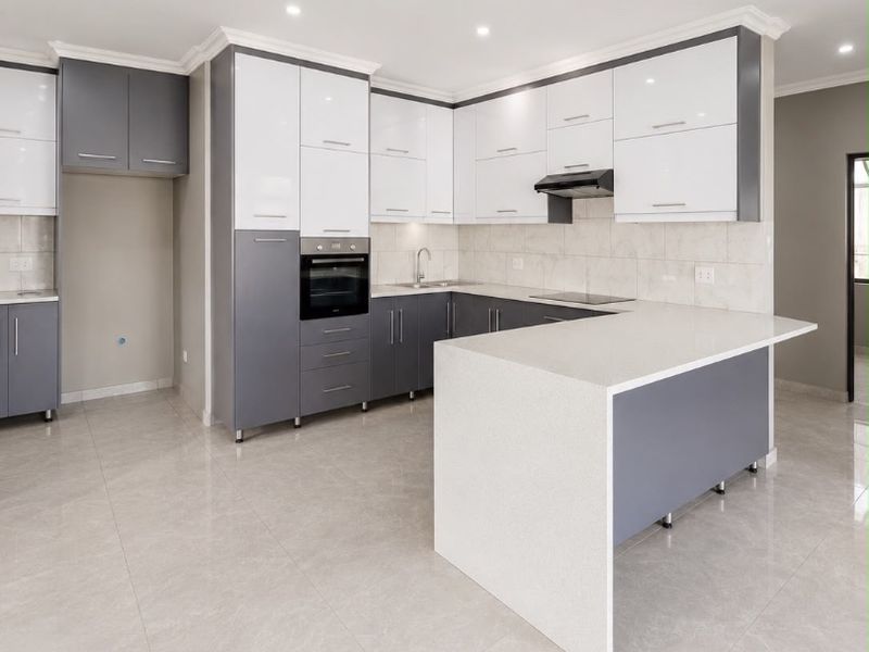 Modern, spacious kitchen featuring high-gloss cabinetry, quartz countertops, a functional island, and integrated appliances, finished with sleek tiled flooring and recessed lighting.