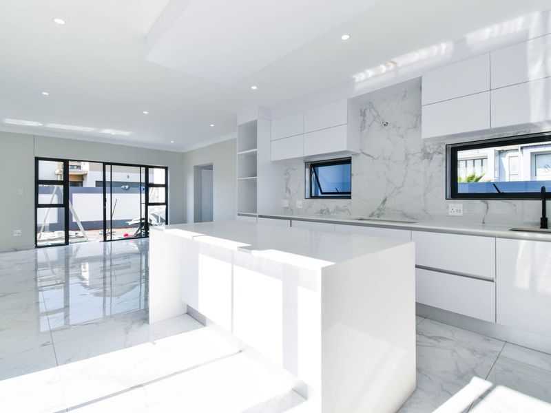 Modern open-plan kitchen and living area featuring high-gloss cabinetry, marble-look finishes, and large sliding doors leading to an outdoor space.