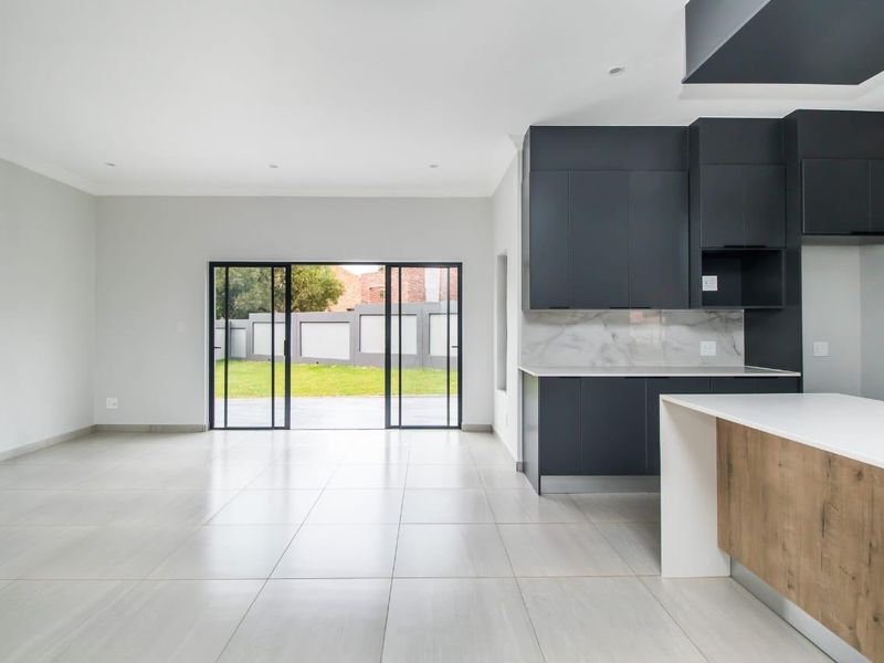 Modern open-plan living and kitchen area featuring sleek dark cabinetry, stone countertops, marble-look splashback, and large sliding doors leading to the garden.