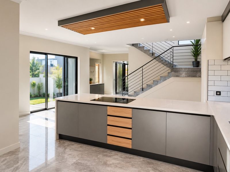 Modern open-plan kitchen featuring a central island with integrated hob, stone countertops, and a striking timber ceiling detail, adjacent to a contemporary staircase.