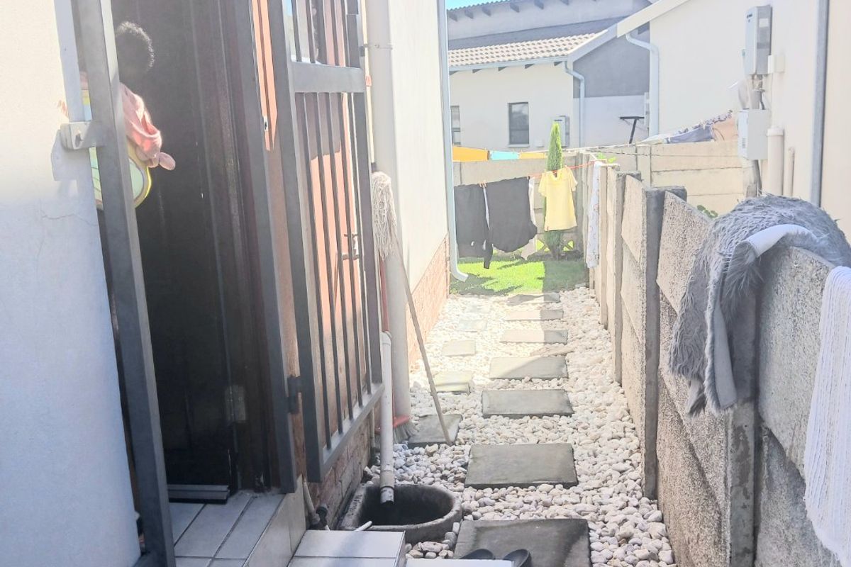A narrow side passage featuring a tiled entrance step, security gate, pebble landscaping, and a precast concrete boundary wall.