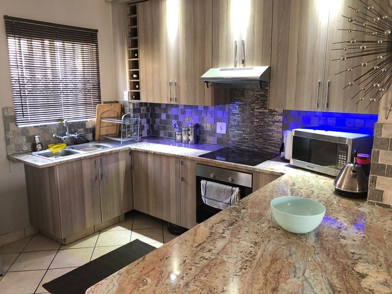 Modern kitchen featuring granite countertops, mosaic tile backsplash, built-in oven, electric hob, and integrated wine rack with under-cabinet lighting.