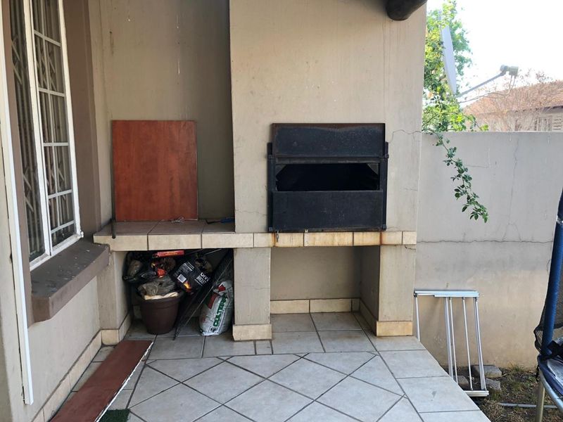 Covered patio area featuring a built-in braai with tiled flooring and masonry structure, requiring some maintenance to the plaster and finishes.