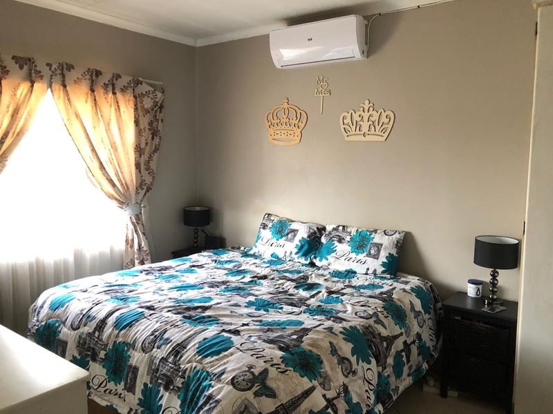 A comfortable bedroom featuring a wall-mounted split-system air conditioner and neutral wall tones, providing a functional space for rest.