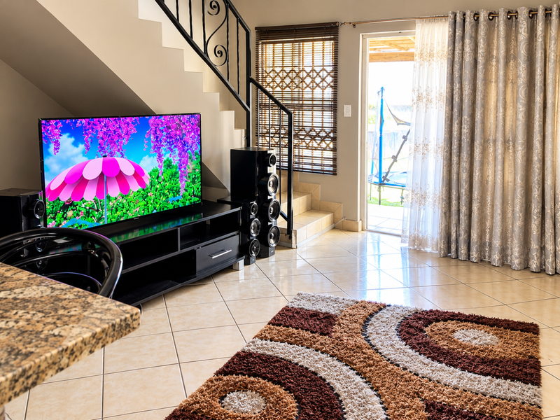 A bright living room featuring tiled flooring, a staircase with a decorative wrought iron balustrade, and direct access to an outdoor patio area.