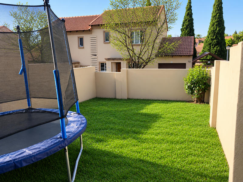 A private rear garden featuring a well-maintained lawn enclosed by high boundary walls, with a view of the townhouse exterior.
