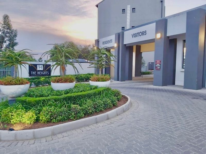 The entrance to The Heights estate featuring a paved driveway, landscaped garden beds, and a modern security gatehouse for residents and visitors.