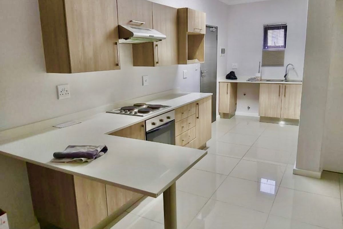 Modern kitchen featuring light wood-finish cabinetry, stone countertops, integrated electric hob and oven, and sleek tiled flooring throughout.