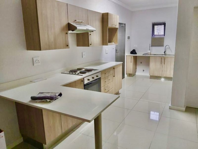 Modern kitchen featuring light wood-finish cabinetry, stone countertops, integrated electric hob and oven, and sleek tiled flooring throughout.