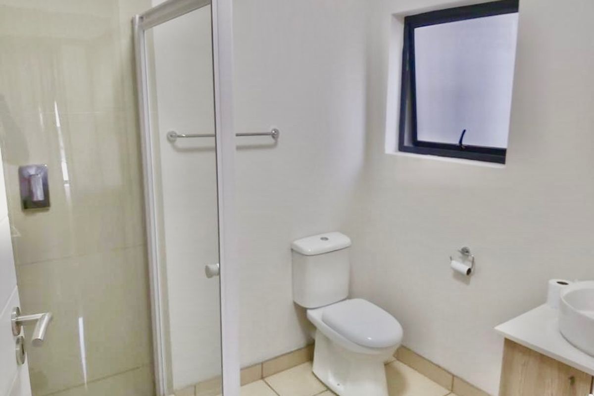 A clean and modern bathroom featuring a glass shower enclosure, a white toilet, and a vanity cabinet with a basin.