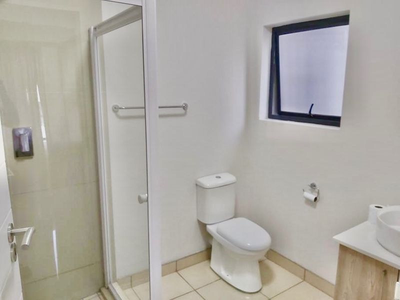 A clean and modern bathroom featuring a glass shower enclosure, a white toilet, and a vanity cabinet with a basin.