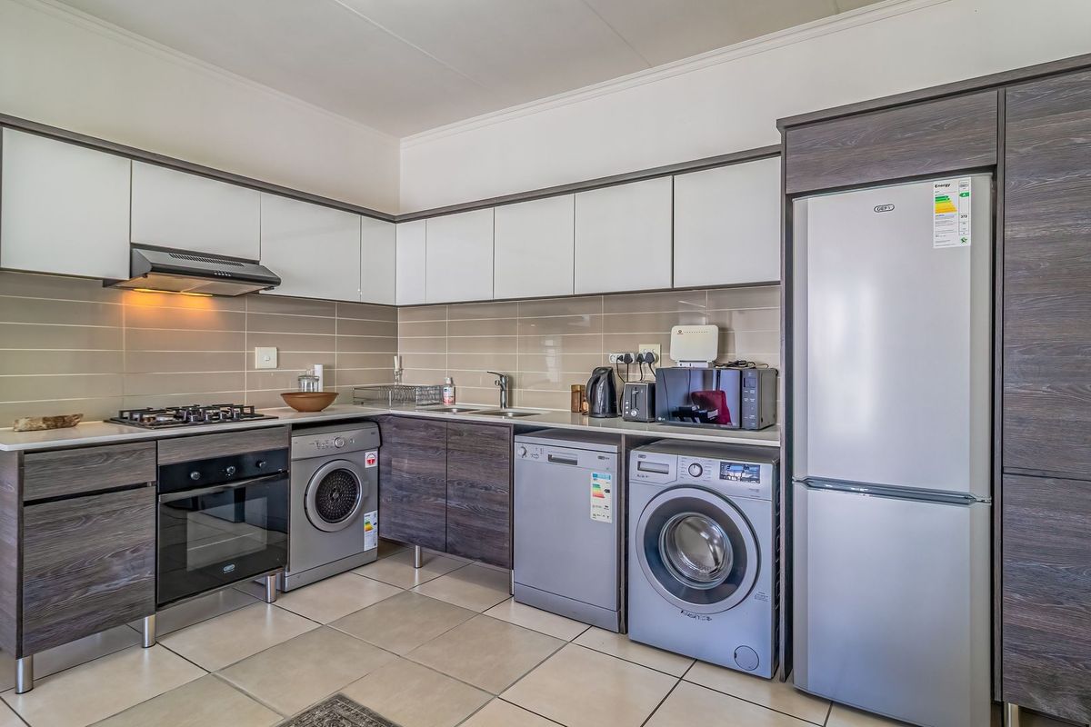 Modern kitchen featuring two-tone cabinetry, gas hob, built-in oven, extractor fan, tiled backsplash, and integrated space for laundry appliances.
