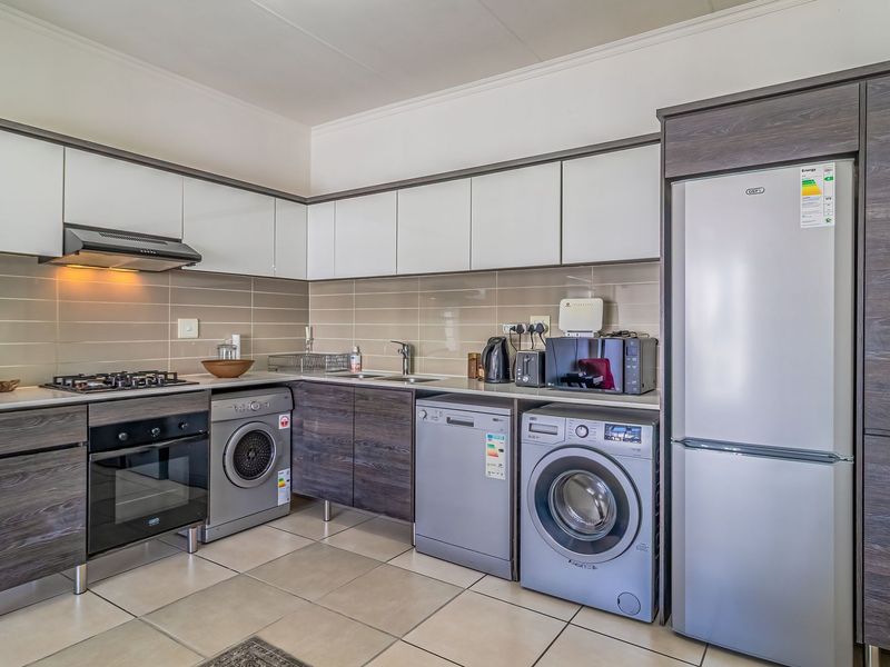 Modern kitchen featuring two-tone cabinetry, gas hob, built-in oven, extractor fan, tiled backsplash, and integrated space for laundry appliances.