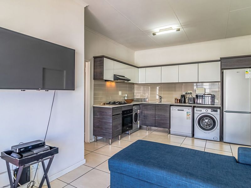 Open-plan living area featuring a modern kitchen with built-in cabinetry, gas hob, oven, extractor fan, and tiled flooring throughout.