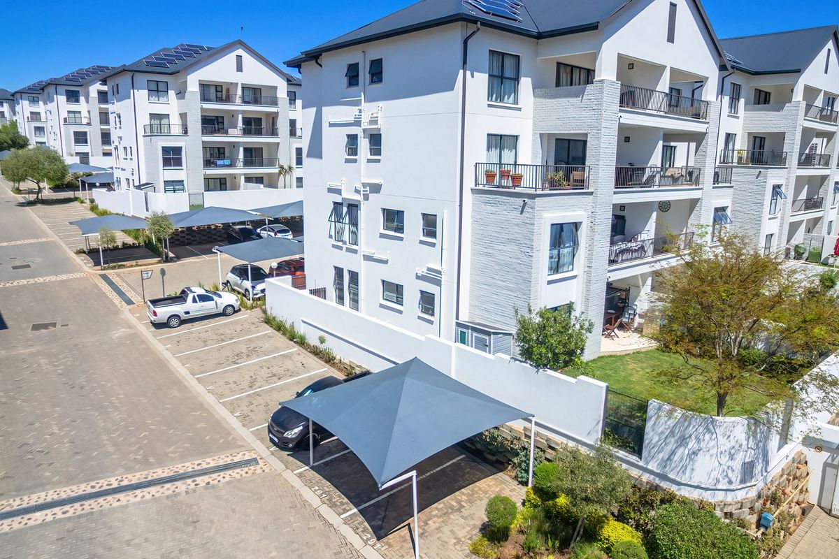 Aerial view of a modern apartment complex featuring paved parking areas with carports, landscaped gardens, and multi-story residential buildings with balconies.