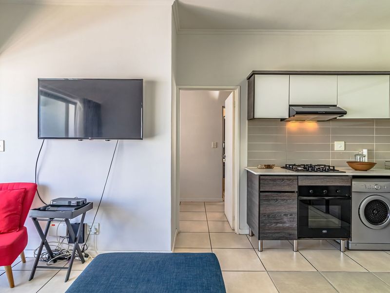 Open-plan living area featuring a modern kitchen with built-in cabinetry, gas hob, oven, extractor fan, and integrated washing machine, finished with tiled flooring.
