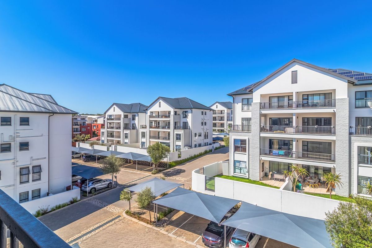 An elevated view of a modern apartment complex featuring paved driveways, covered parking structures, and multi-story residential buildings with private balconies.