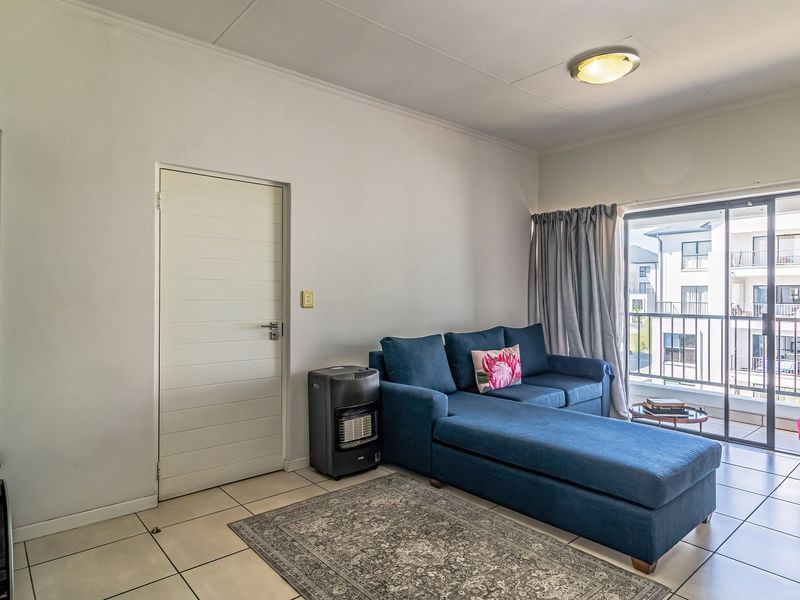 A bright living room featuring tiled flooring and a sliding glass door providing access to a private balcony.