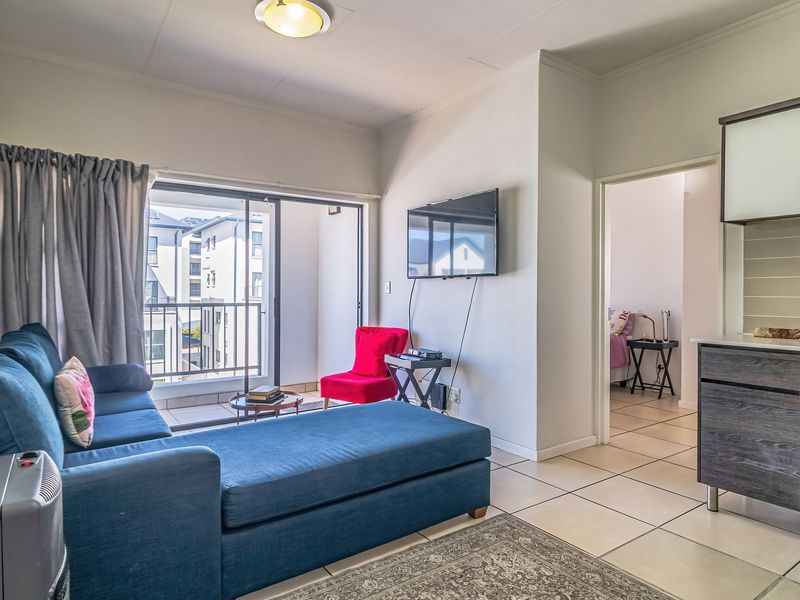 Open-plan living area featuring a modern kitchen with built-in appliances, tiled flooring, and direct access to a private balcony through sliding glass doors.