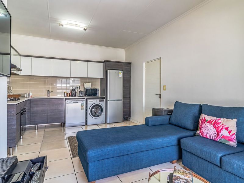 An open-plan living area featuring a modern kitchen with built-in cabinetry, tiled flooring, and integrated appliances, seamlessly connected to the lounge space.