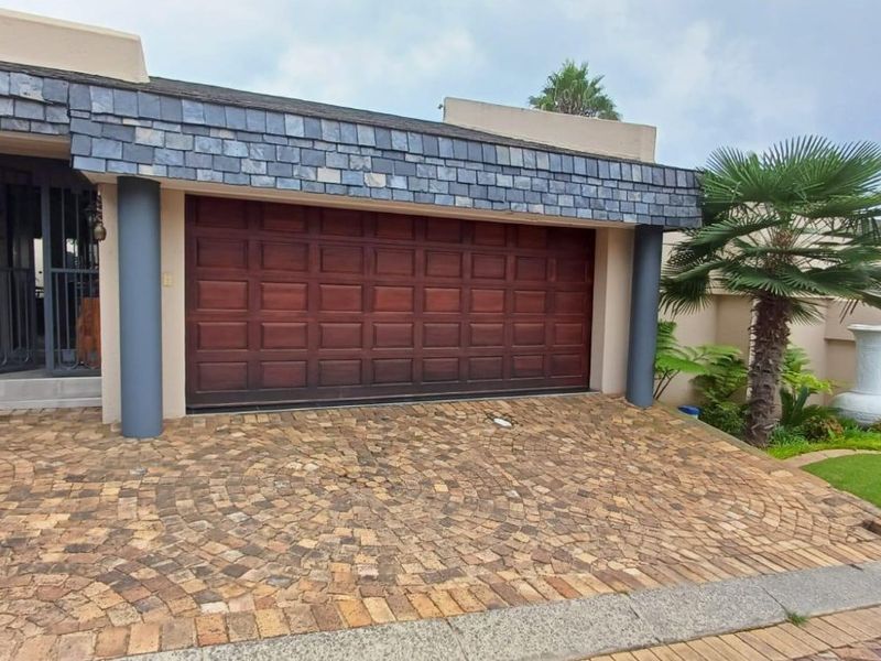 Front elevation featuring a double garage with wooden door, cobblestone driveway, and distinctive slate roof detailing.
