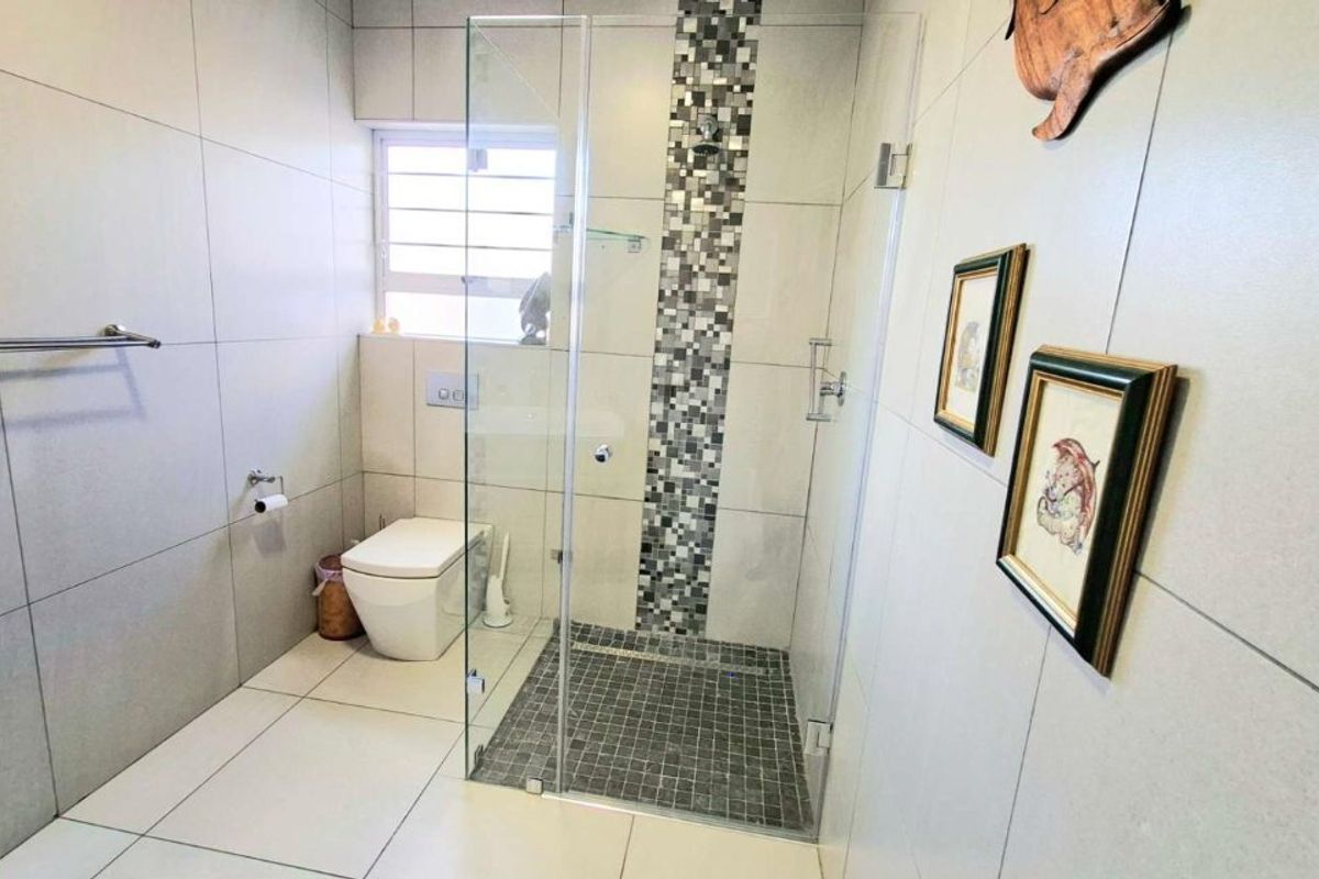 Modern bathroom featuring a walk-in shower with glass enclosure, mosaic tile accents, and a wall-hung toilet with neutral ceramic tiling throughout.