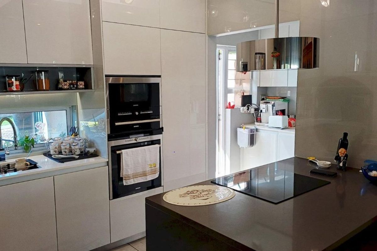 Modern kitchen featuring high-gloss cabinetry, stone countertops, integrated appliances including an oven, microwave, and induction hob, with a sleek central island.