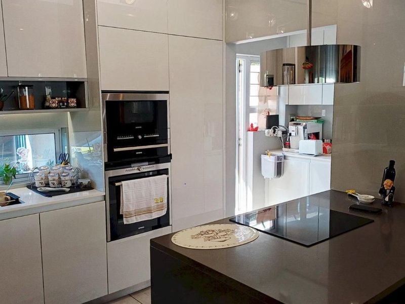 Modern kitchen featuring high-gloss cabinetry, stone countertops, integrated appliances including an oven, microwave, and induction hob, with a sleek central island.