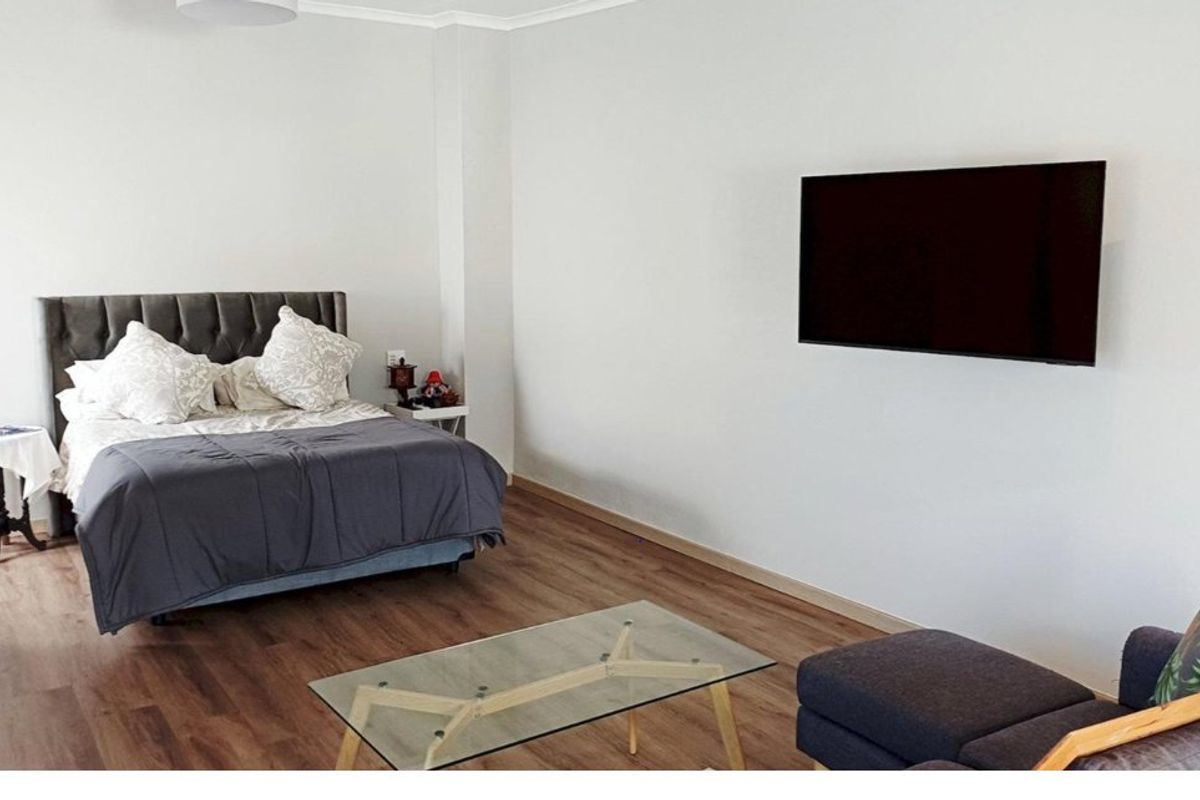 A spacious bedroom featuring modern laminate flooring and a wall-mounted television, offering a clean and neutral living space.
