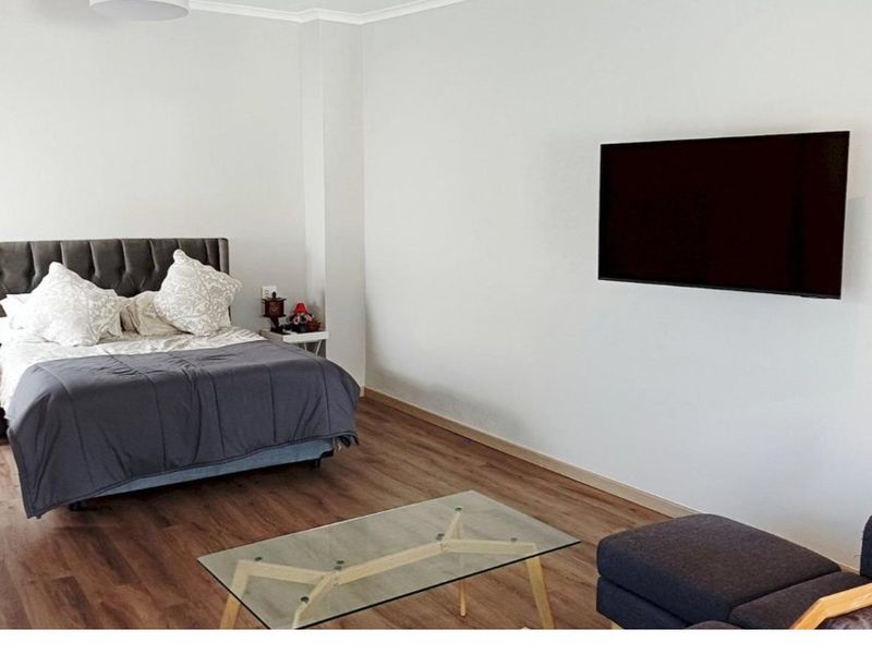 A spacious bedroom featuring modern laminate flooring and a wall-mounted television, offering a clean and neutral living space.