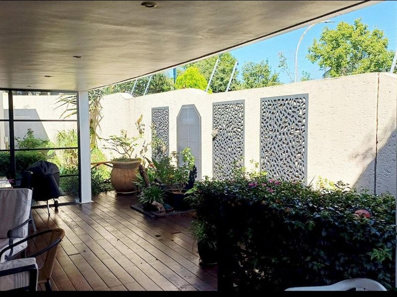 A well-maintained covered patio featuring timber decking, recessed lighting, and decorative privacy screens set against a secure boundary wall.