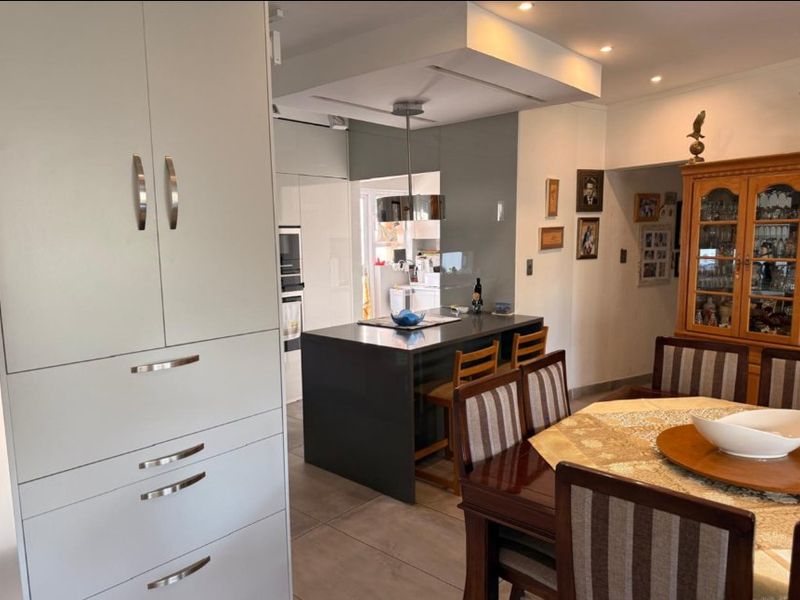 Modern open-plan kitchen and dining area featuring a central island, sleek cabinetry, recessed lighting, and tiled flooring throughout.
