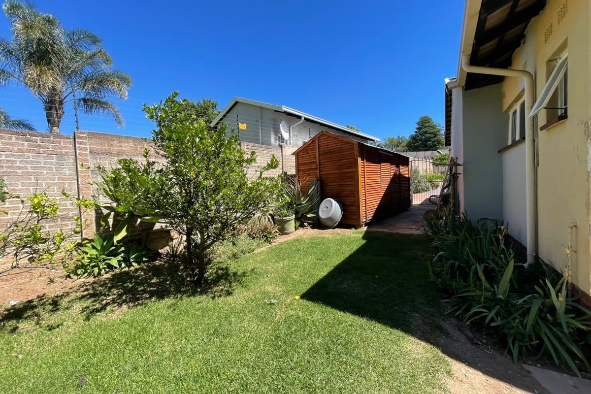 A rear garden area featuring a lawn, a wooden storage shed, and brick boundary walls with electric fencing.