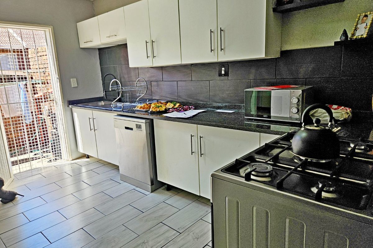 Modern kitchen featuring white cabinetry, granite countertops, tiled backsplash, and integrated appliances, with direct access to an outdoor area.
