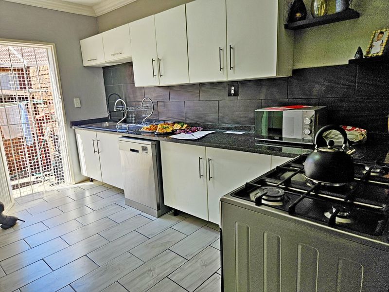 Modern kitchen featuring white cabinetry, granite countertops, tiled backsplash, and integrated appliances, with direct access to an outdoor area.