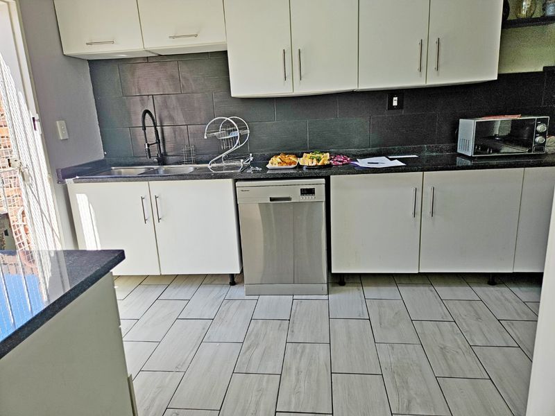 Modern kitchen featuring white cabinetry, dark granite countertops, a tiled backsplash, and a stainless steel dishwasher with light wood-look floor tiles.