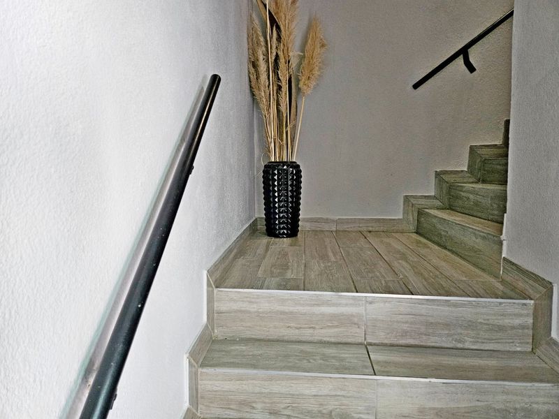 A clean, modern staircase featuring wood-look tiled steps and a sleek black metal handrail.