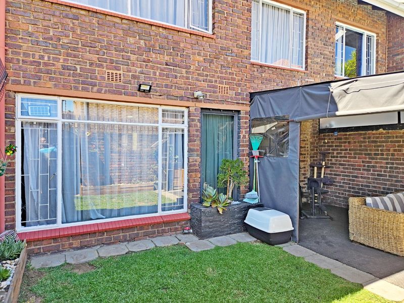 Rear exterior view of the townhouse featuring a face brick facade, large windows with security bars, and a covered patio area with canvas enclosure.