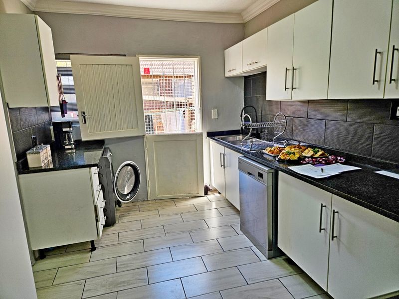 Functional kitchen featuring white cabinetry, dark granite countertops, tiled backsplash, and integrated dishwasher with direct access to the exterior.