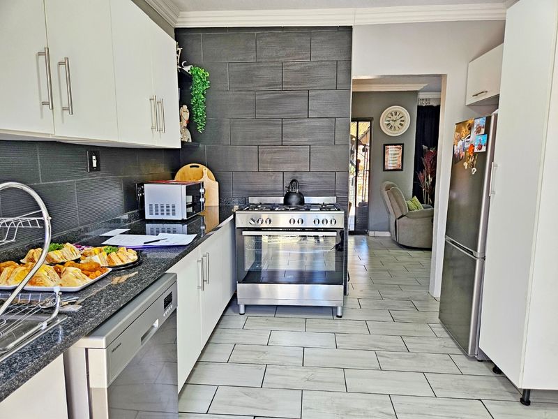 Modern kitchen featuring sleek white cabinetry, granite countertops, stainless steel gas stove, and contemporary tiled backsplash with direct access to the living area.