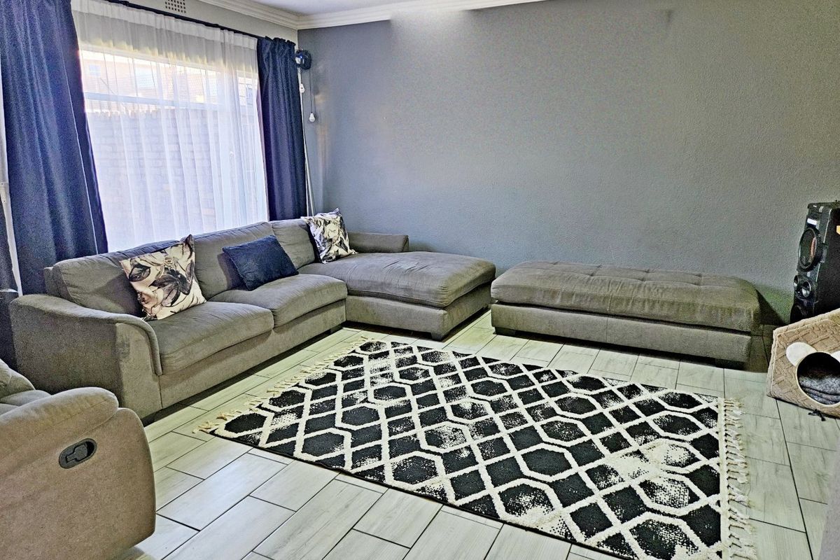 A well-maintained living room featuring light-colored tiled flooring, crown molding, and a large window allowing for natural light.